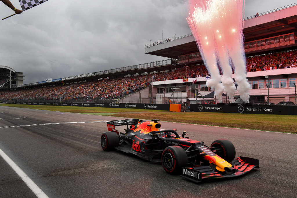 A Formula 1 car crosses the finish line as fireworks explode behind.