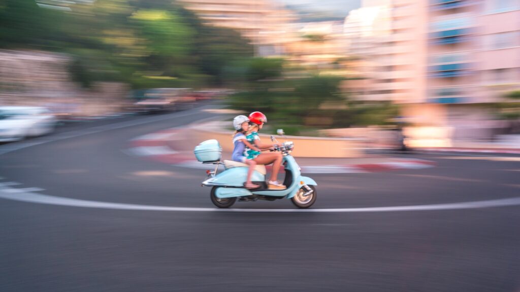Two people riding a Vespa scooter around the Fairmont hairpin in Monaco