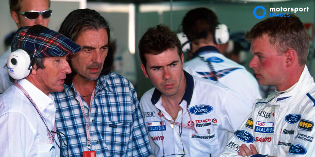 George Harrison is given a tour of a Formula 1 garage
