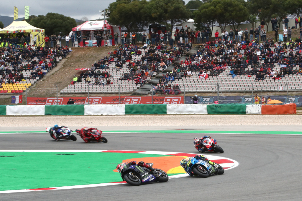 Five MotoGP riders ride their bikes around a corner in front of a grandstand in Portugal